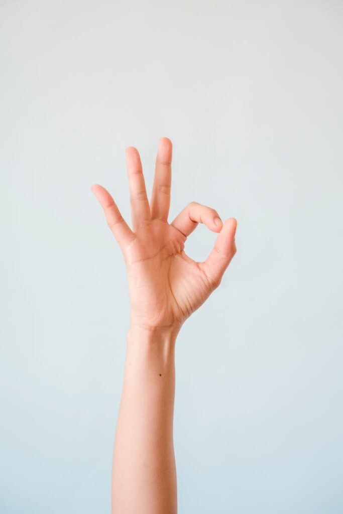 A single human hand making an OK gesture, isolated against a soft pastel background.