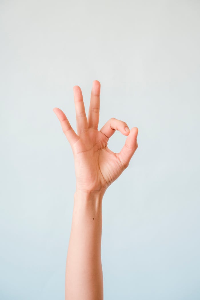 A single human hand making an OK gesture, isolated against a soft pastel background.